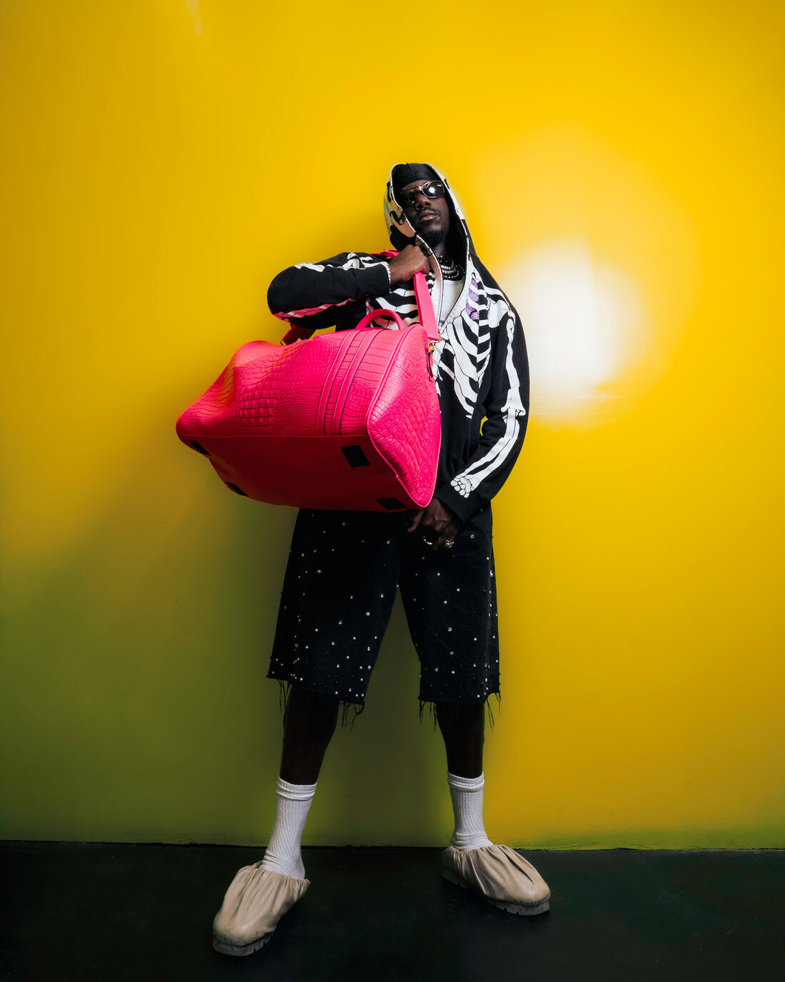 A man in a skeleton jacket holding a coral Tote&Carry duffle against a yellow wall